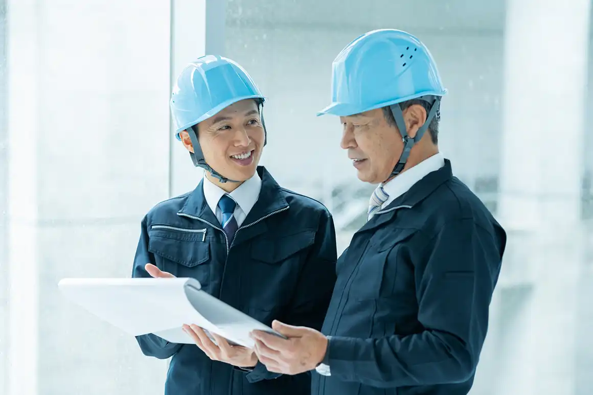 青いヘルメットを着用した作業服姿の2人が書類を確認する様子