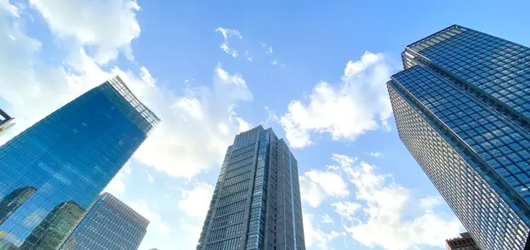 青い空と都会のビル群を見上げる