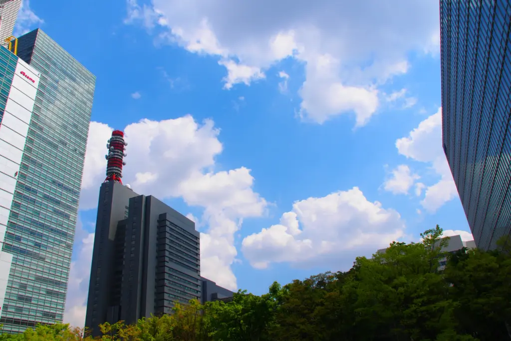 高層ビルと青空、手前には緑の木々の都市景観